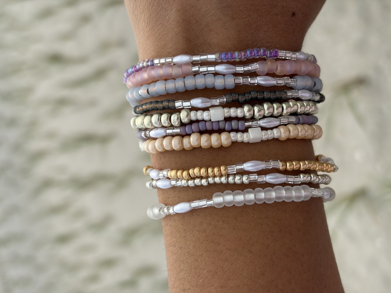 A stack of handmade bracelets on a wrist by the sand